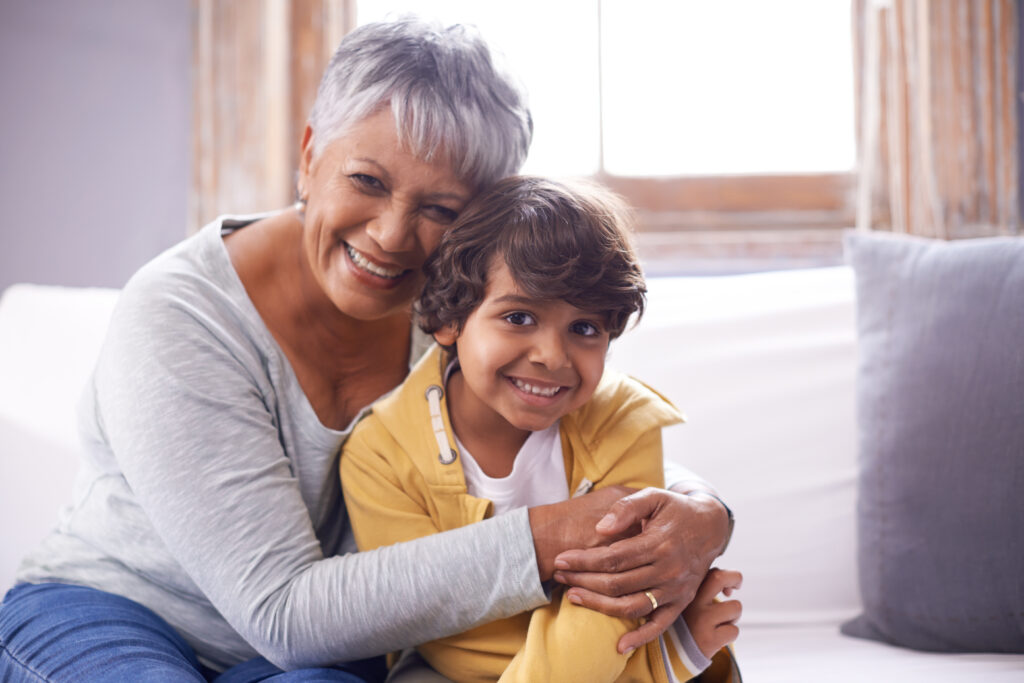 A grandmother hugging her smiling grandson on the couch